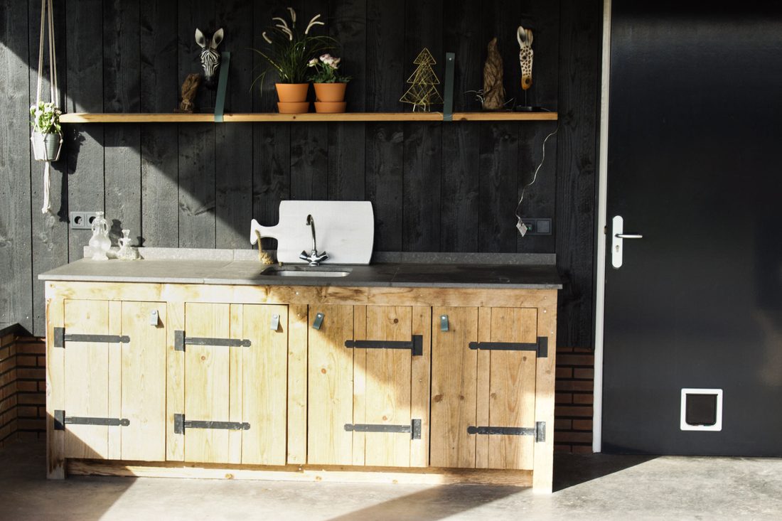 Buitenkeuken van steigerhout met betonnen blad tegen een zwarte houten wand